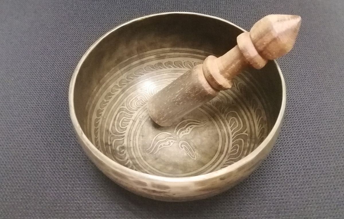 Metallene Klangschale mit Klöppel auf hellem Untergrund
